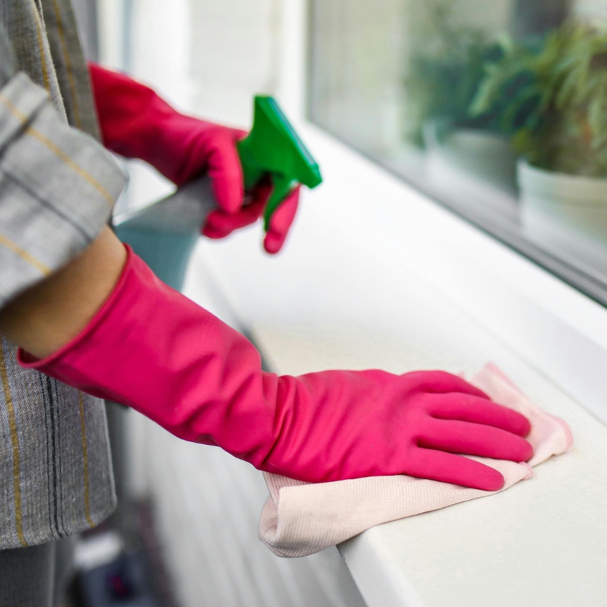 Person wearing pink gloves cleaning a surface with a cloth and green spray bottle.