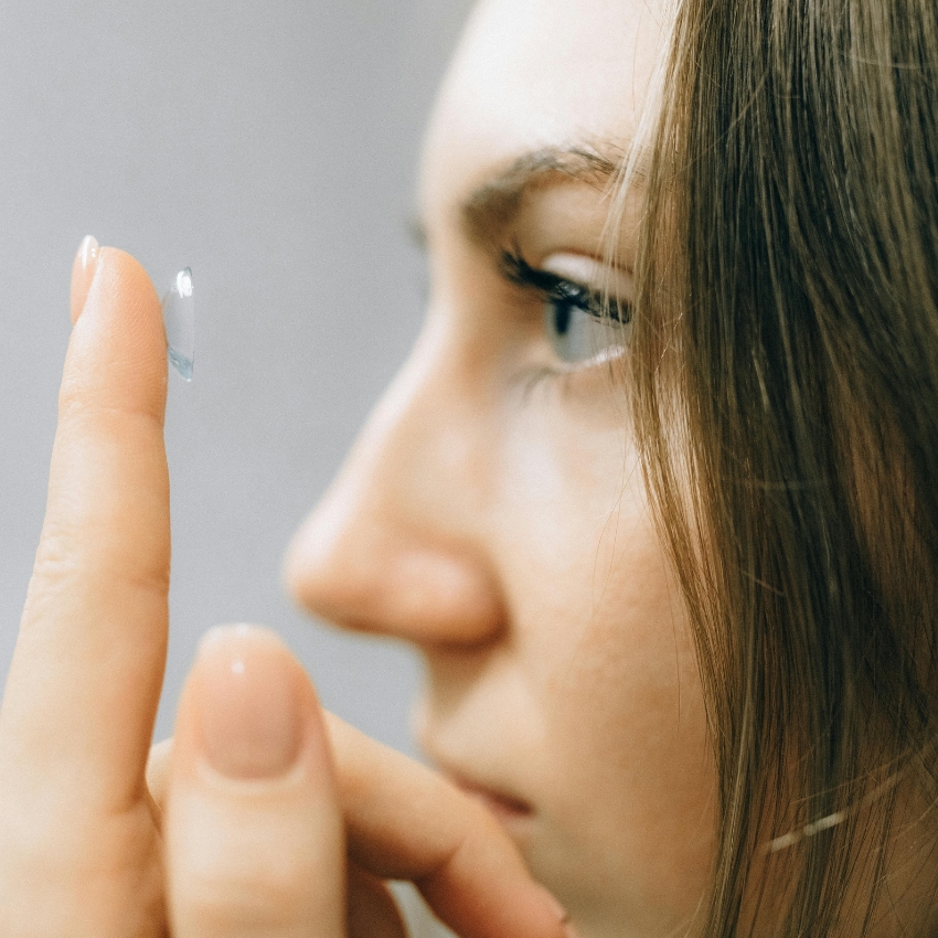 Woman holding a contact lens on her fingertip near her eye.