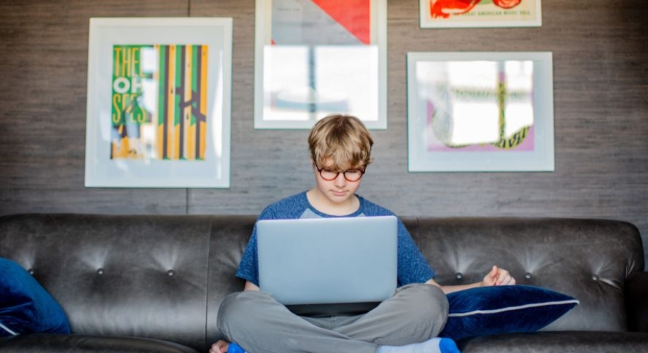 Teenager sitting cross-legged on a sofa using a laptop.