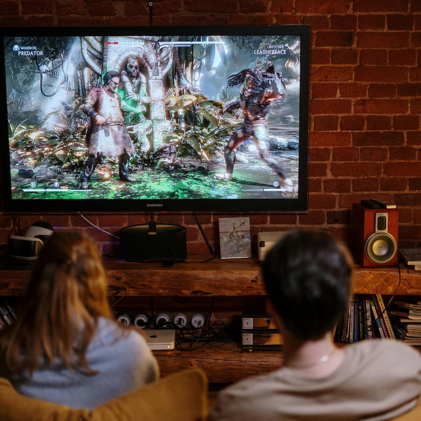 Two people watching a video game on a Samsung TV. Characters: Predator vs. Leatherface.