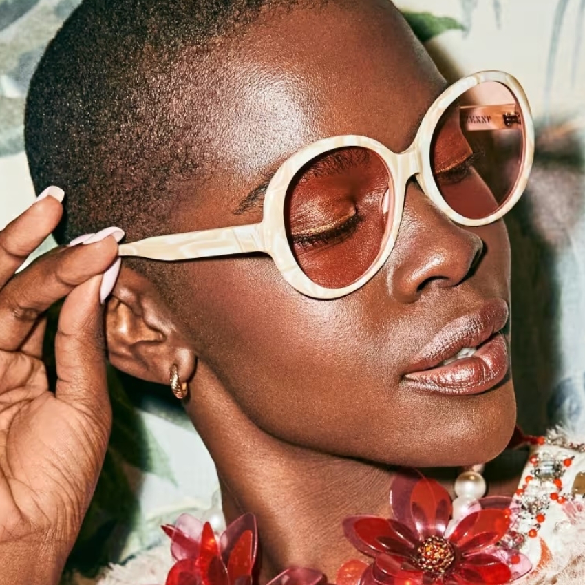 Cream sunglasses with round pink lenses worn by a person.