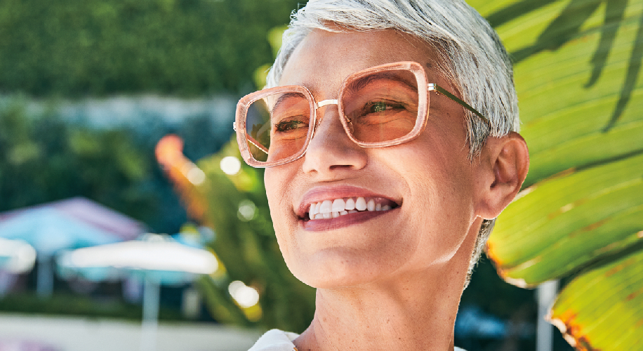 Woman smiling while wearing square, oversized, pink-tinted sunglasses.