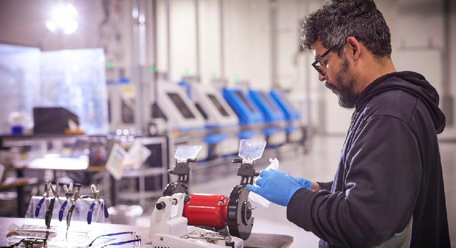 Man working with industrial equipment in a factory, holding tools and wearing gloves.