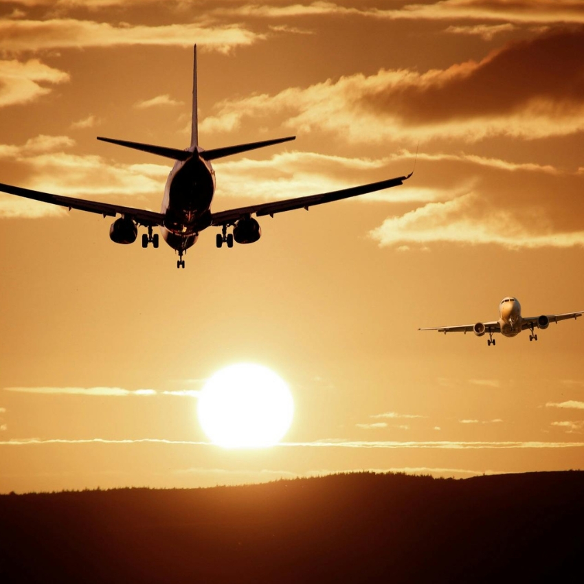 Two airplanes flying towards a sunset sky.