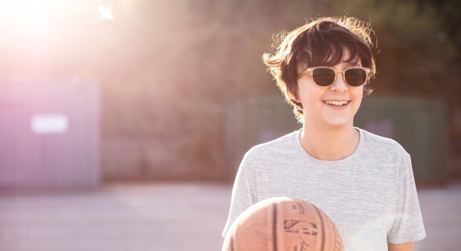 Youth wearing sunglasses holds a basketball and smiles.
