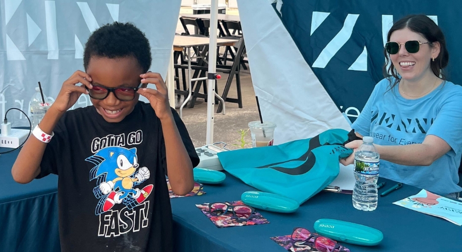 Child trying on glasses with Zenni Volunteer at Right Back At Ya Event.