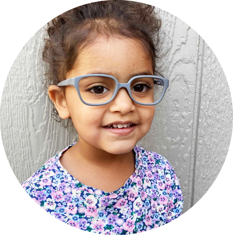 Image of a little girl wearing grey plastic frames and smiling.