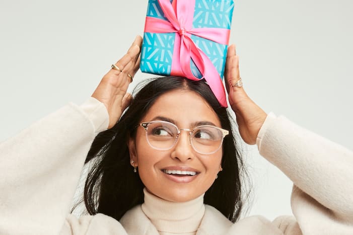 Image shows a woman wearing glasses with a brightly wrapped gift on her head.