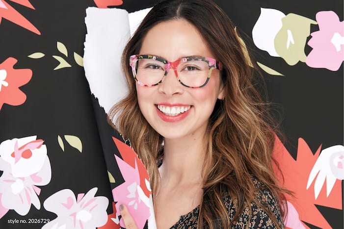 Image of a woman smiling wearing Zenni square glasses #2026729, ripping through patterned paper that matches her glasses.