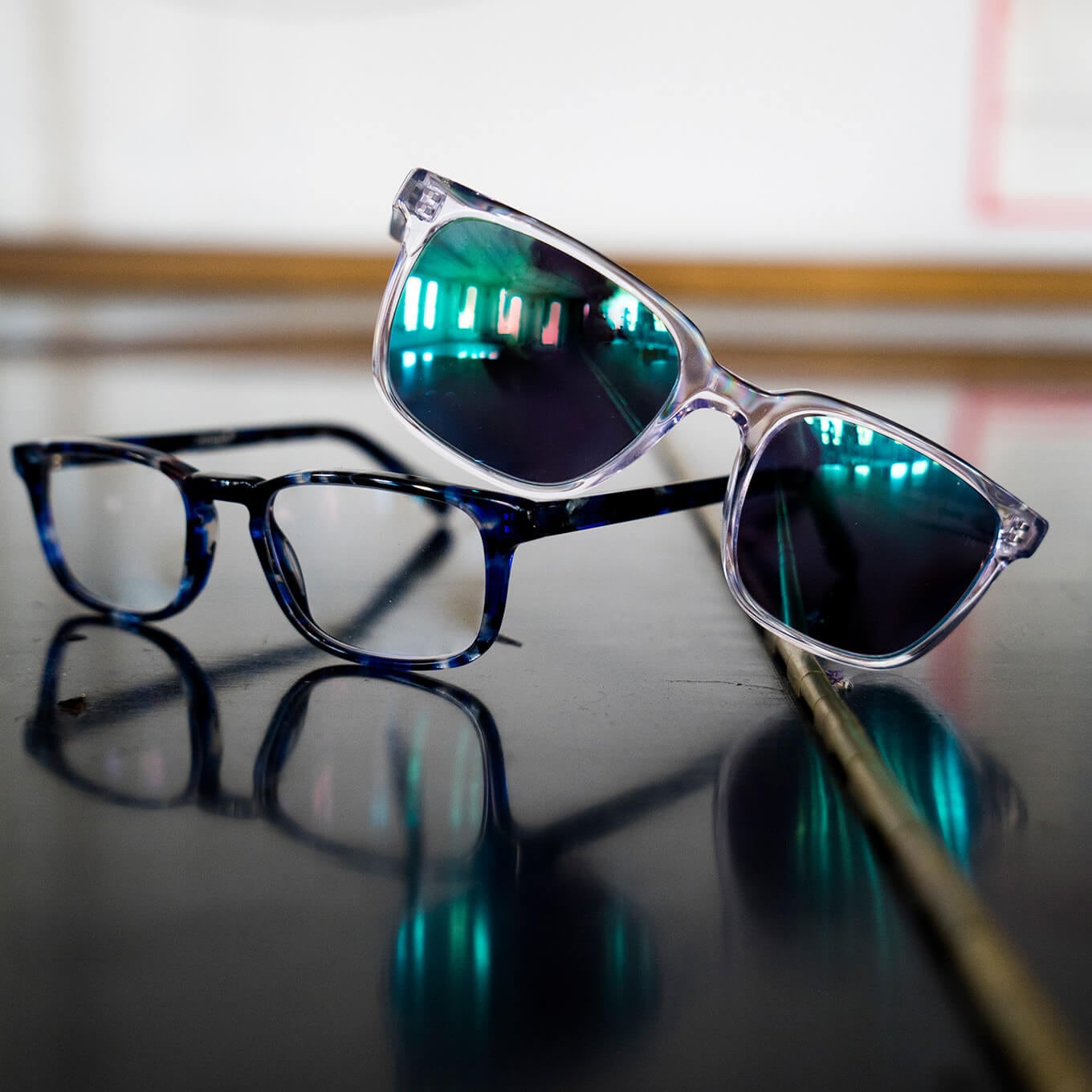 Translucent Van Alen sunglasses with green mirror tint and blue tortoiseshell Eames rectangle eyeglasses from the Zenni Metropolitan Collection are pictured together.
